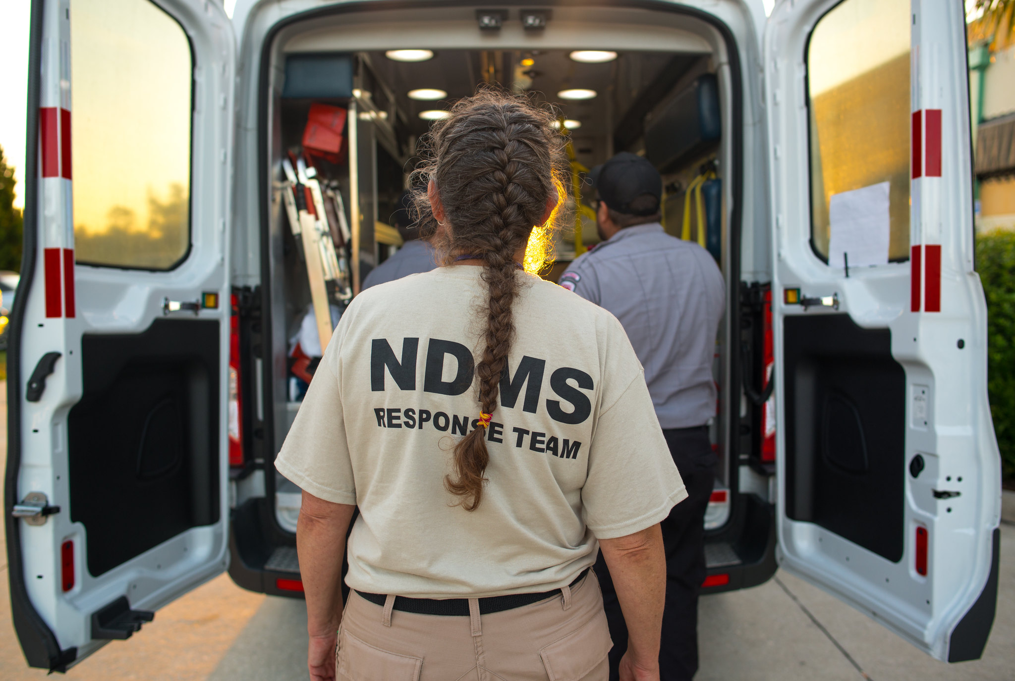Lady wearing NDMS t-shirt facing the back of an Ambulance