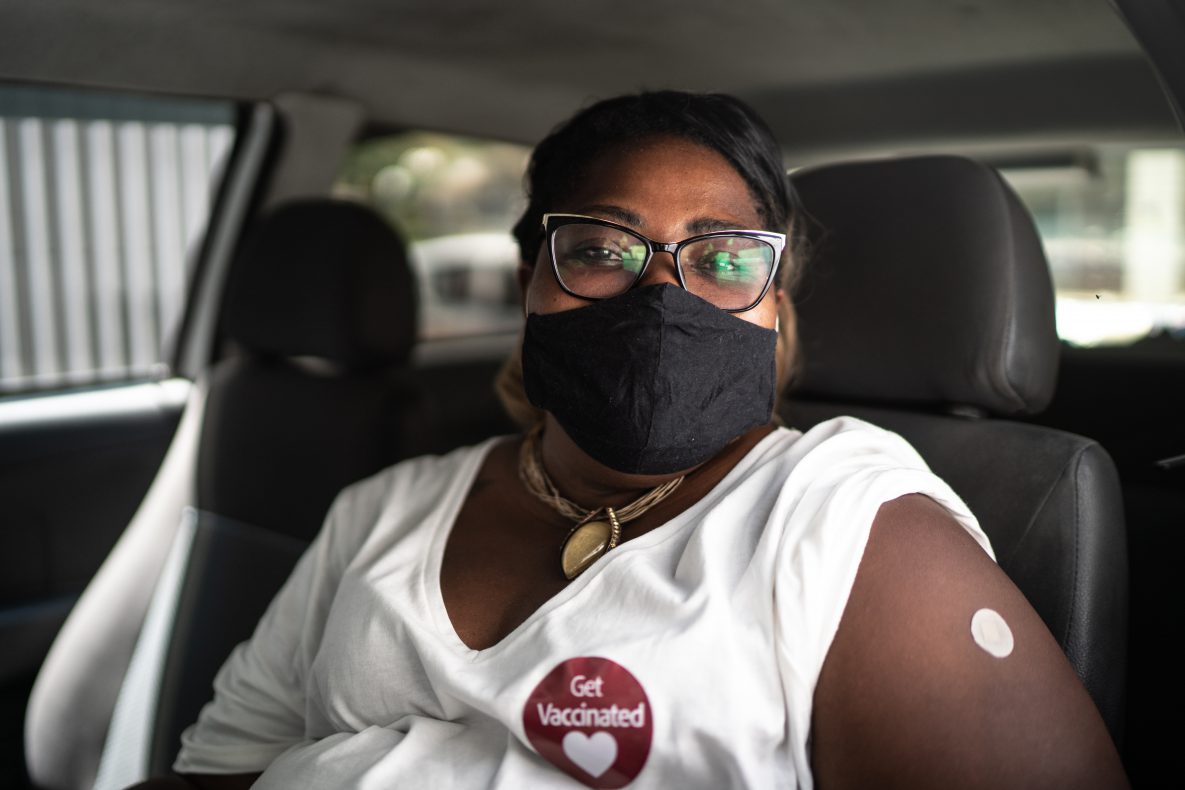 Portrait of a happy woman in a car with a 'get vaccinated' sticker - wearing face mask