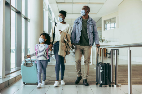 Parents and child wearing masks, walking with suitcases through airport.