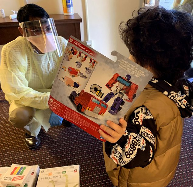 A medical officer wearing PPE giving a toy to a child in quarantine