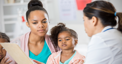 Mother and doctor reviewing an informed consent form while young daughter looks on 