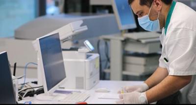 A person standing in front of a computer, wearing a surgical mask