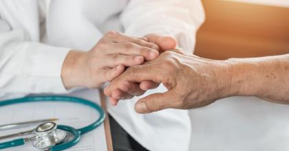 Geriatric doctor holds the hand of an elderly senior adult patient in medical office during examination.