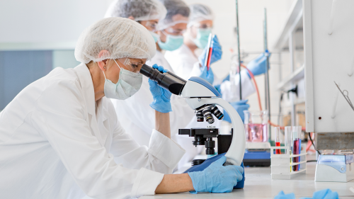 laboratory scientist wearing full personal protective gear seated at bench looking into microscope conducting medical research