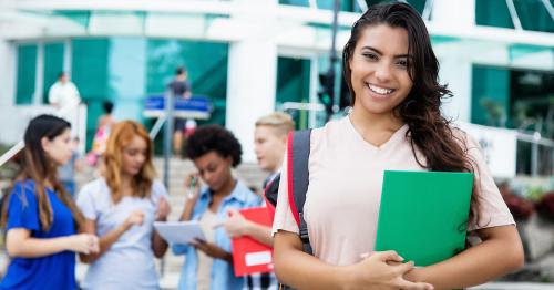 Smiling female college student in foreground, group of students on campus in background