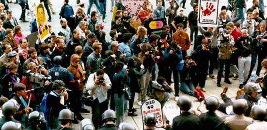 Crowd holding protest signs facing a line of police in riot gear