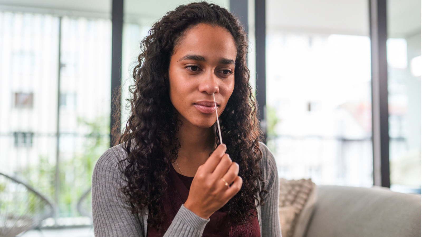 A woman performing a nose swab on herself as part of a COVID at home test.