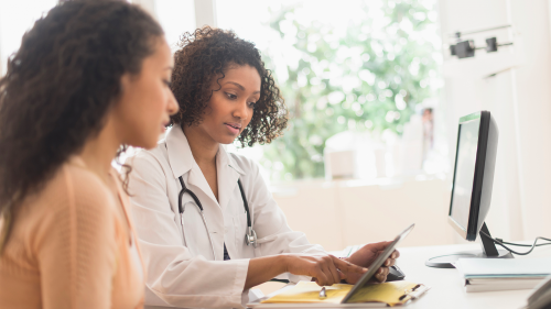 African-American woman speaking to African-American female doctor at desk in doctor's office