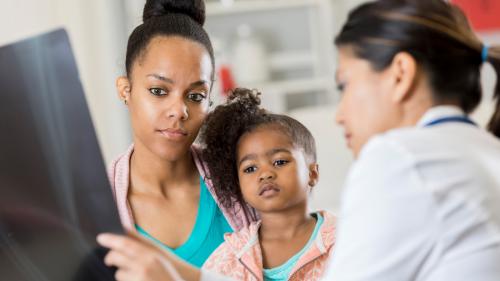 A doctor showing an X-ray print to a mother and child.