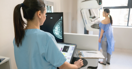 a nurse giving a patient a mammogram including the image of the patient's breast on the computer monitor