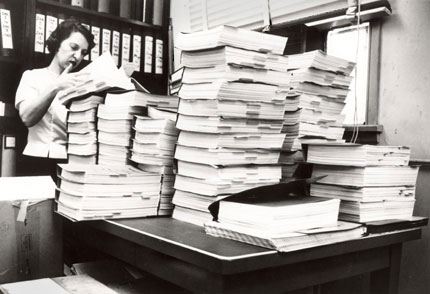 A woman looking over several binders of information housed on a lab table.