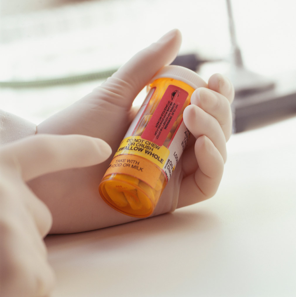 Photo of  a person holding prescription bottle of pills, pointing at label, Close-up of hands