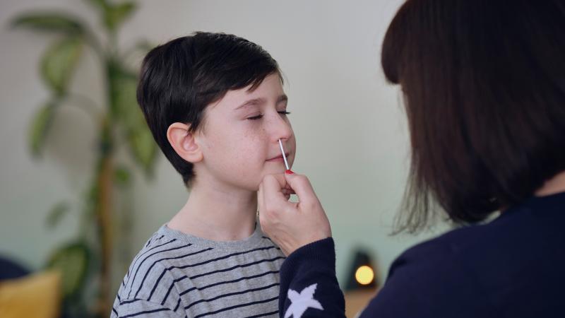Adult taking a sample from a child’s nose for a COVID-19 at-home test.