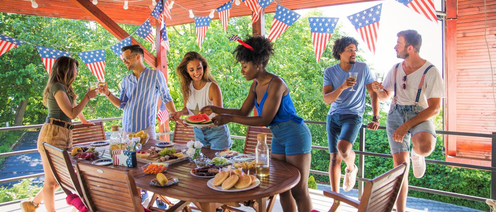 Group of people having an outside party with food displayed on the table in a shaded area.