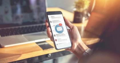 Hand holding smartphone with new email notification, with computer in background