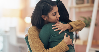 Two young women hugging while at home.