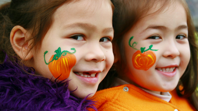 two smiling young girls wearing halloween costumes with pumpkins painted on their faces