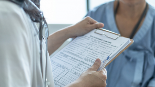 Image of a doctor speaking with a patient. A clipboard is the focal point of the picture.