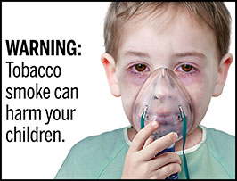 A rectangular cigarette health warning with a white background and black text that reads: “WARNING: Tobacco smoke can harm your children.” To the right of the text is a photorealistic illustration showing the head and shoulders of a young boy (aged 8-10 years) wearing a hospital gown and receiving a nebulizer treatment for chronic asthma resulting from secondhand smoke exposure. The warning is surrounded by a black outline.