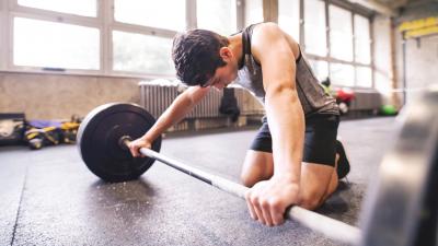 teen gripping barbell as it sits on the gym floor