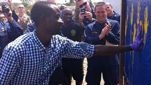 U.S. Public Health Service officers celebrate as a Liberian man adds his handprint to a “survivors’ wall.” Each patient who overcame Ebola after treatment at the USPHS mobile hospital outside Monrovia was given a set of clothes and essentials and invited to mark their recovery with a handprint. (Photo: FDA)