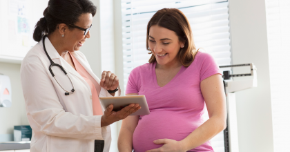 Photo of female health care specialist talking with pregnant woman in exam room.