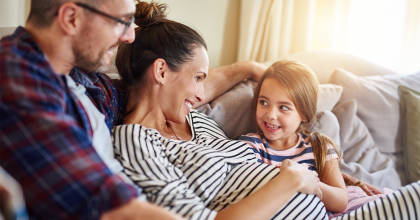 Family on couch with the young girl rubbing her pregnant mother's belly