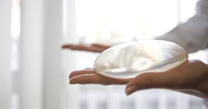 Photograph of a woman holding a breast implant