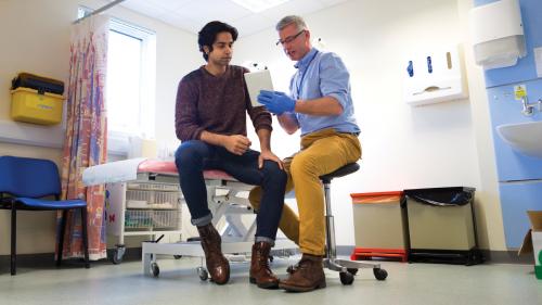 young male patient conversing with doctor in examining room while looking at iPad