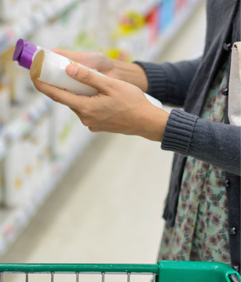 Image of woman in supermarket comparing shampoos.