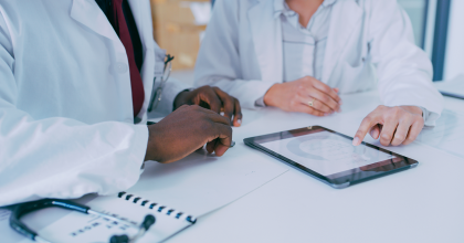 Photo of two doctors sitting at desk looking at iPad.