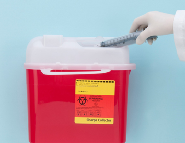 Syringe being placed into red sharps disposal container with biohazard label.