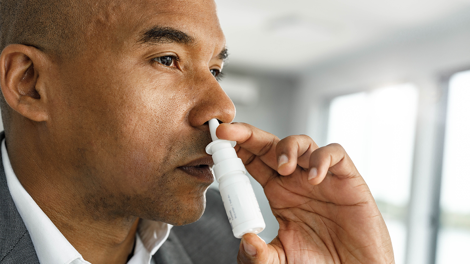 A man holding nasal spray canister in one hand, and inserting canister tip into nose. 