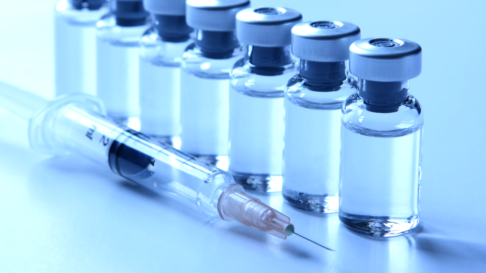 a row of seven small glass medical vials containing clear liquid and a medical syringe used for injecting vaccines