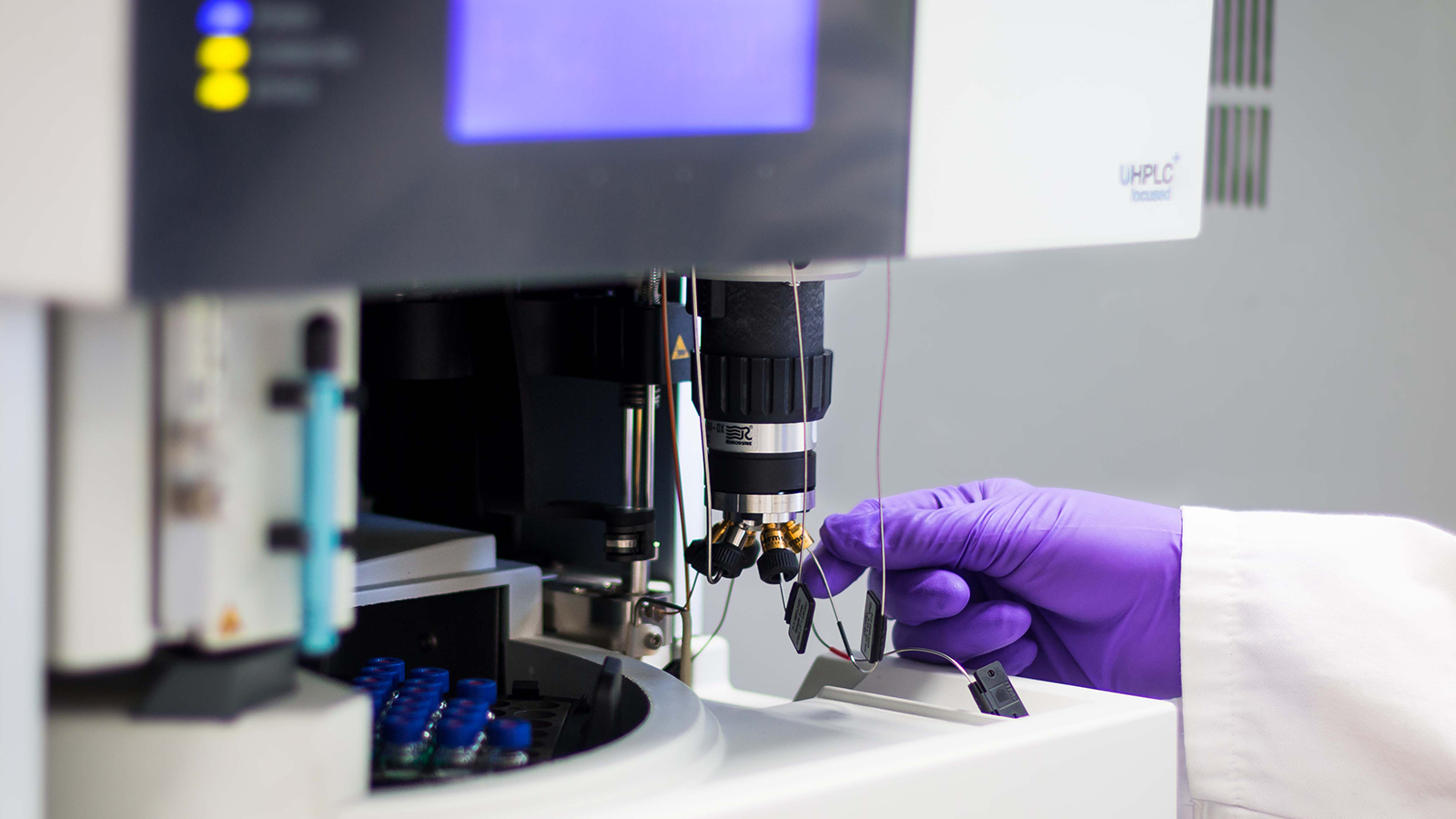 A scientist wearing purple gloves using a mass spectrometer