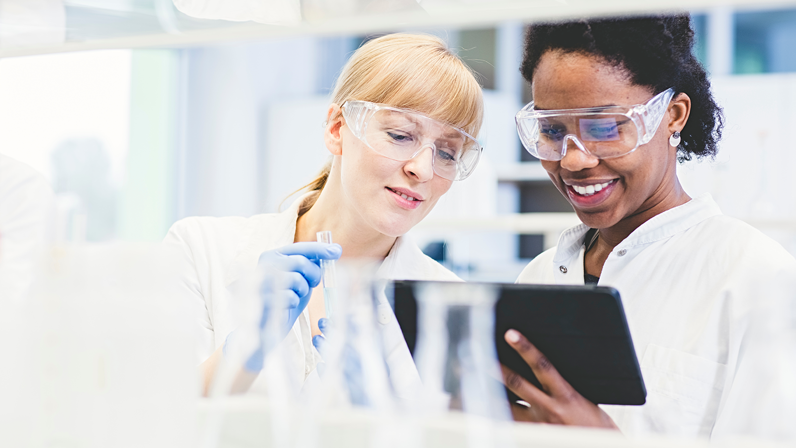 Two female scientists wearing goggles consulting on lab results