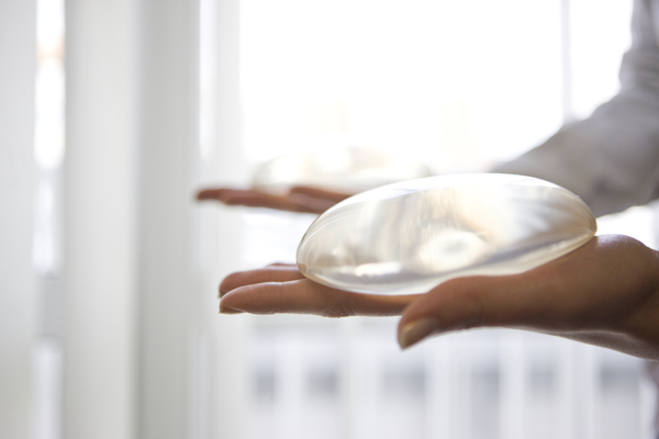 Photograph of a woman holding a breast implant