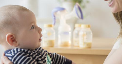 photo of mother holding infant with breast milk bottles in the background