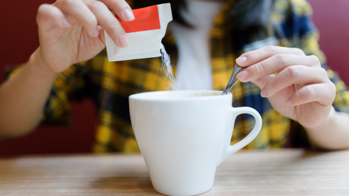 Sugar substitutes. Image of woman pouring sugar substitute into her cup of coffee/tea.