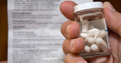 Person holding a glass bottle of pills and a medication guide