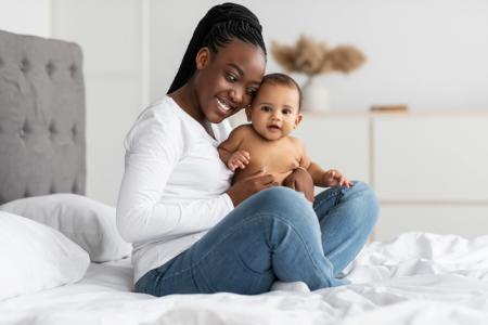 Black mom sitting on bed with infant