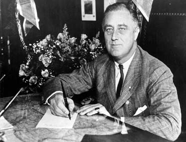 President Roosevelt sitting at a desk signing a paper