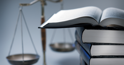 An open book on top of a stack of books with a set of scales in the background