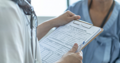 Image of a doctor speaking with a patient. A clipboard is the focal point of the picture.