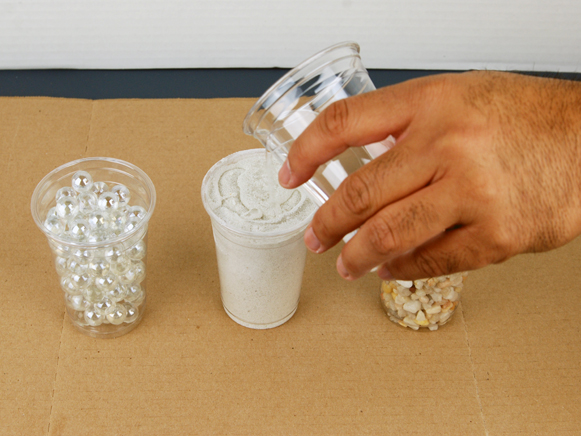 Water being poured in cup of sand and cup of marbles