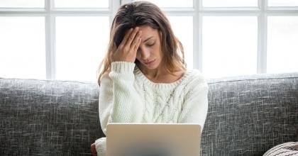 Frustrated woman worried about problem sitting on sofa with laptop.