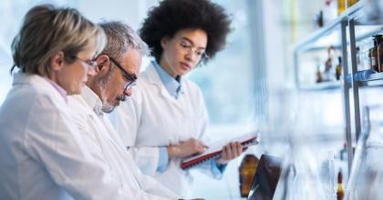 Image of three scientists in white coats in a laboratory reviewing data on a laptop