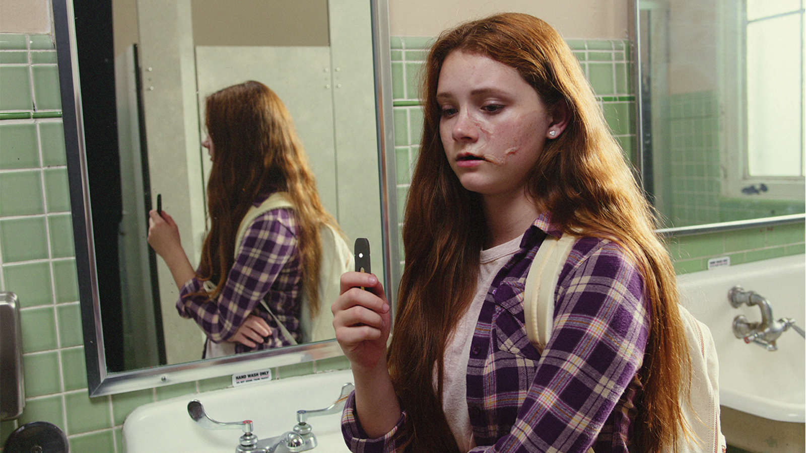 teenage girl holding and looking at a vaping device 