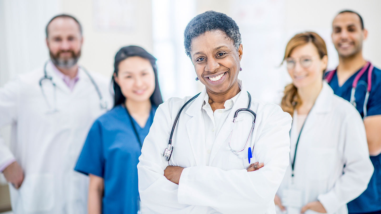 Two male and three female doctors wearing scrubs posing for the camera.