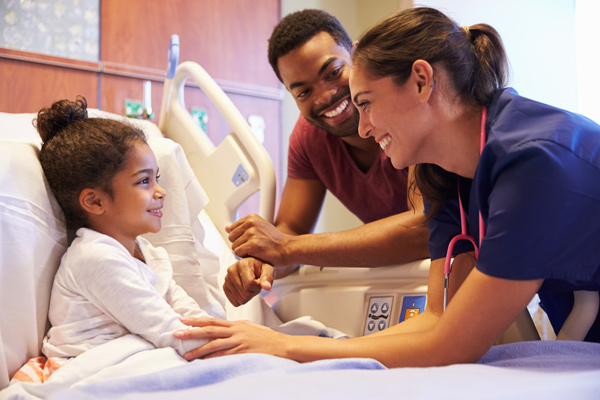 nurse and father tending to child in hospital bed (600x400)